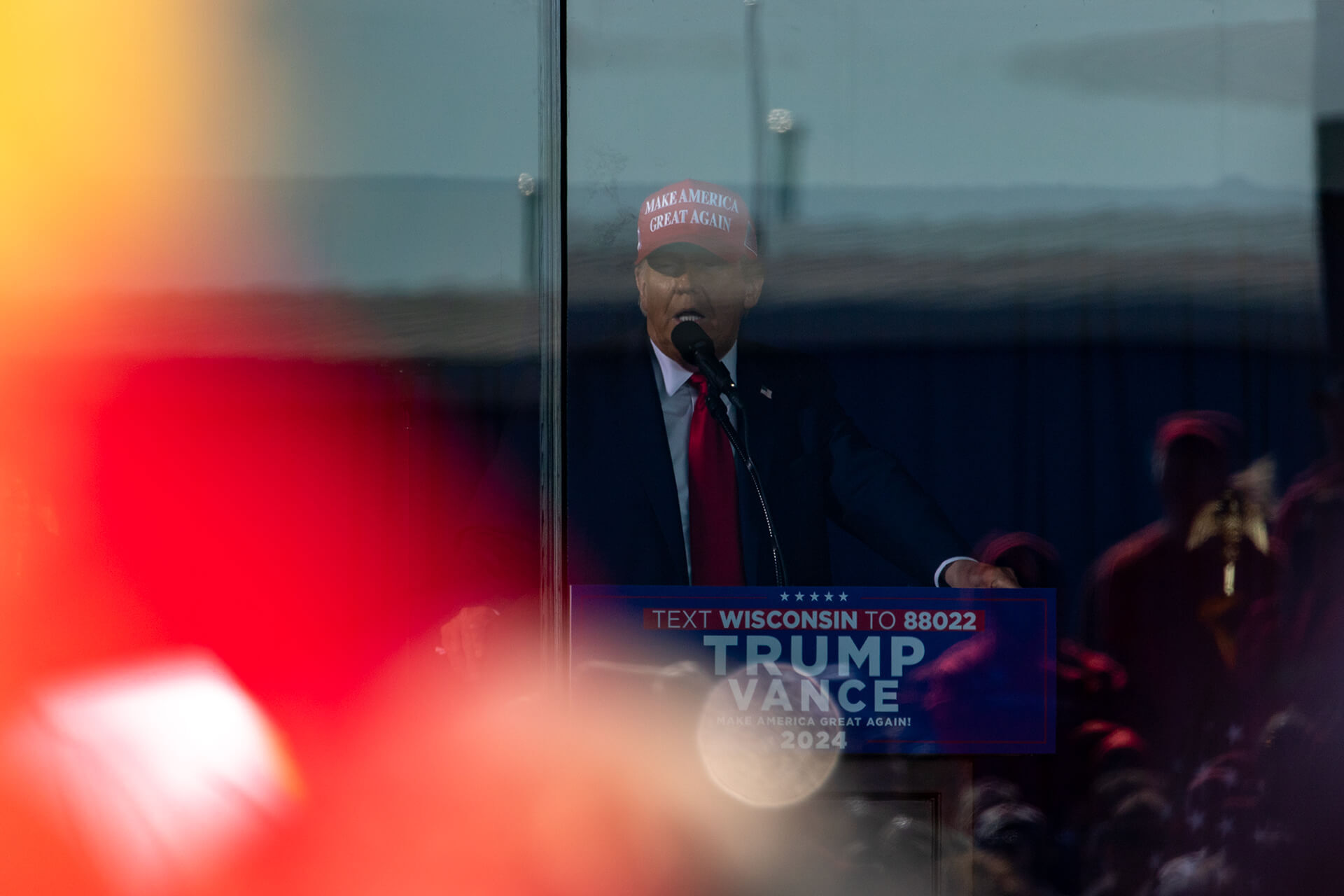 Trump standing behind very reflective ballistic glass.